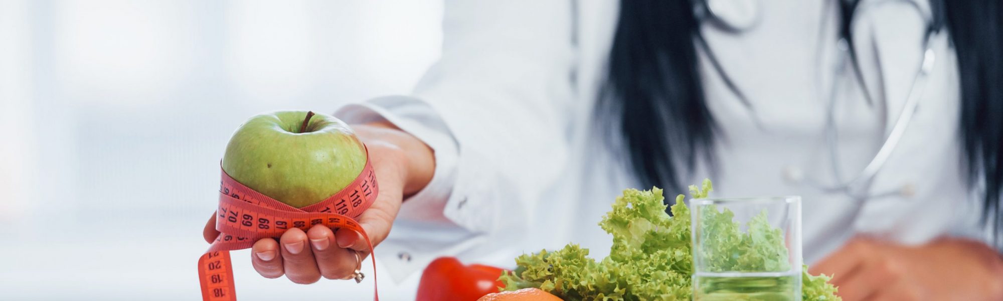 female-nutritionist-white-coat-holding-apple-with-measuring-tape-min